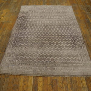 Muted taupe rug with a repeating floral pattern rests on worn honey-colored hardwood floorboards.