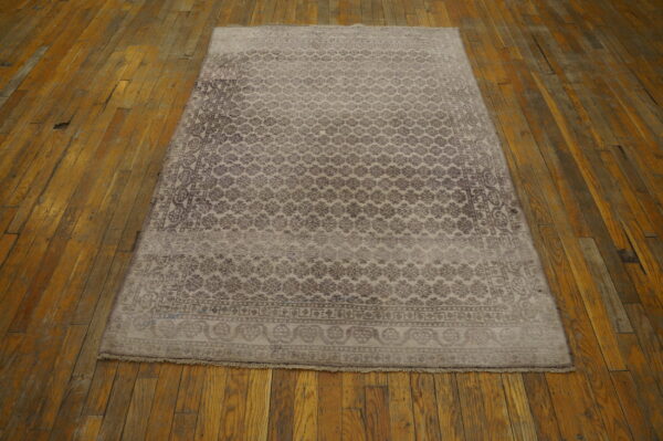 Muted taupe rug with a repeating floral pattern rests on worn honey-colored hardwood floorboards.