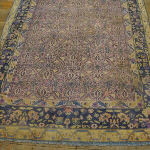Faded pink and yellow low-pile rug with blue geometric designs and floral borders on a rustic wood floor.
