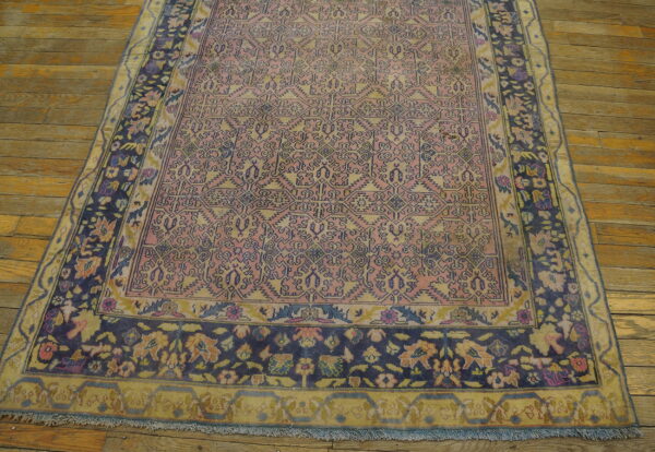 Faded pink and yellow low-pile rug with blue geometric designs and floral borders on a rustic wood floor.