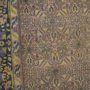 Dusty rose rug with geometric indigo and muted gold patterns, bordered by dark floral designs on wood.