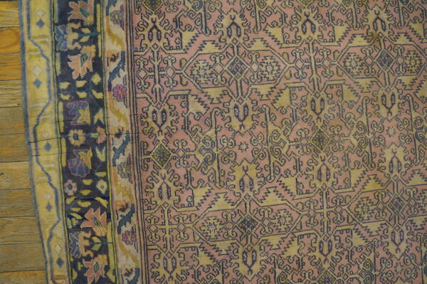 Dusty rose rug with geometric indigo and muted gold patterns, bordered by dark floral designs on wood.