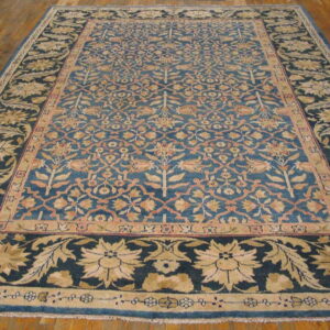 Ornate blue rug with detailed gold and peach floral patterns displayed on a brown hardwood floor.