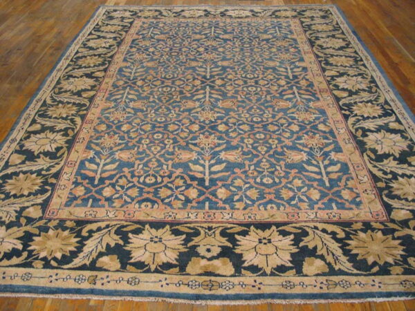 Ornate blue rug with detailed gold and peach floral patterns displayed on a brown hardwood floor.