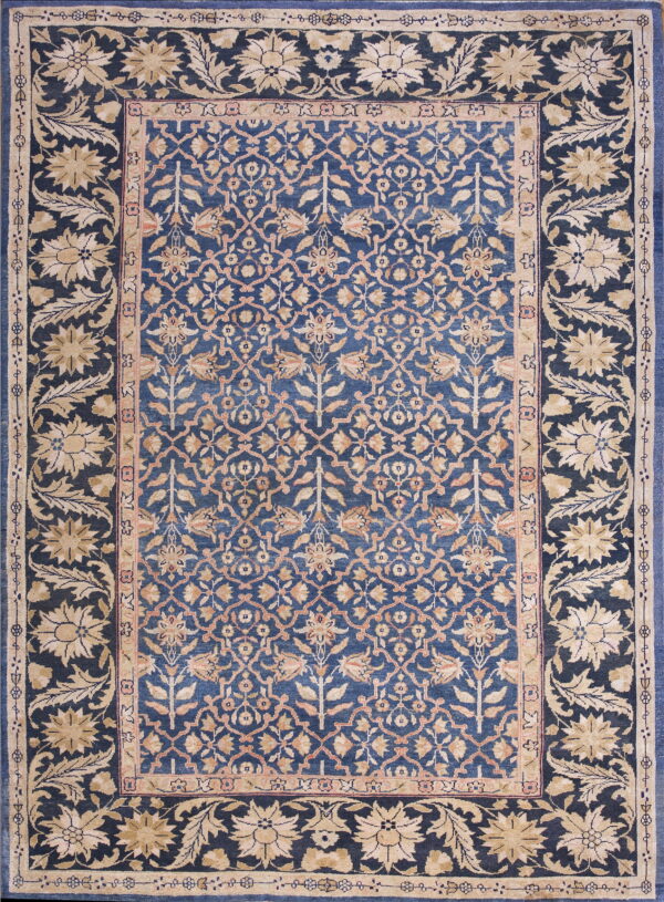 Ornate rug with a deep blue field and beige floral motifs bordered by large stylized flowers.