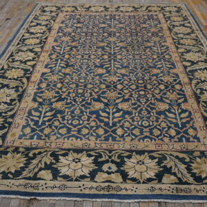 Ornate blue rug with dense floral patterns in gold and salmon laid on rustic hardwood floorboards.