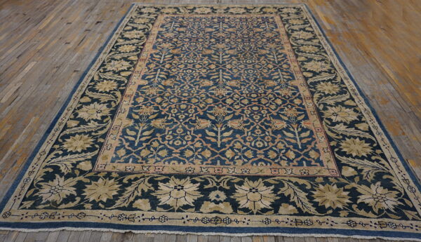 Ornate blue rug with dense floral patterns in gold and salmon laid on rustic hardwood floorboards.