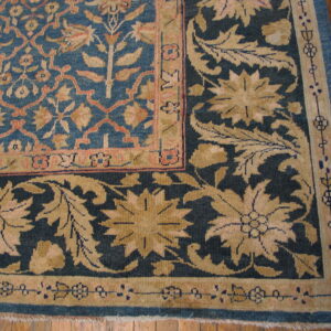 Detail of a blue and beige floral rug corner with contrasting borders over polished wood floors.