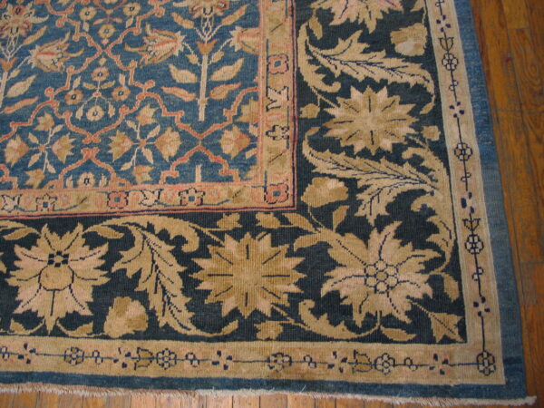 Detail of a blue and beige floral rug corner with contrasting borders over polished wood floors.
