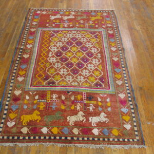 A rust-colored pictorial rug with a geometric center and animal motifs rests on wooden plank flooring.