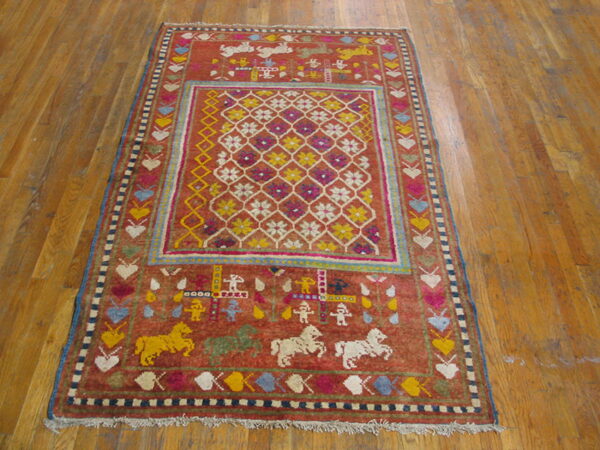 A rust-colored pictorial rug with a geometric center and animal motifs rests on wooden plank flooring.