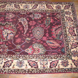 Maroon and cream traditional rug with complex floral designs on light brown hardwood flooring.