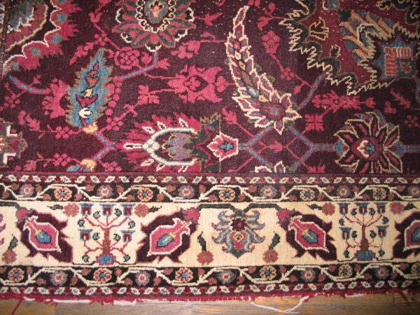 Detail of a low-pile rug with a burgundy field and cream border displaying stylized floral motifs on wood flooring.