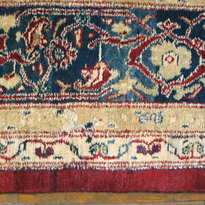 Detailed view of a low-pile rug border featuring blue, red, and beige patterns over hardwood planks.