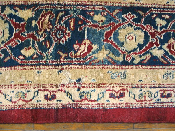 Detailed view of a low-pile rug border featuring blue, red, and beige patterns over hardwood planks.