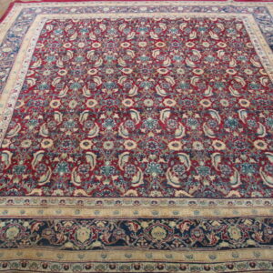 A traditional rug with a burgundy field and detailed blue and cream floral paisley borders, displayed on wood floor.