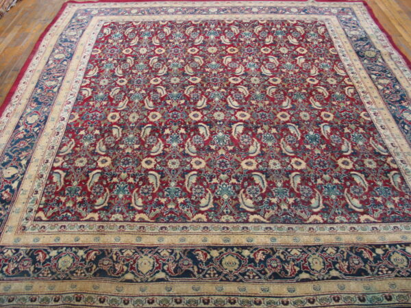 A traditional rug with a burgundy field and detailed blue and cream floral paisley borders, displayed on wood floor.