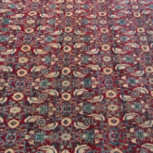 A traditional patterned rug featuring a red background with dense blue, teal, and cream motifs.