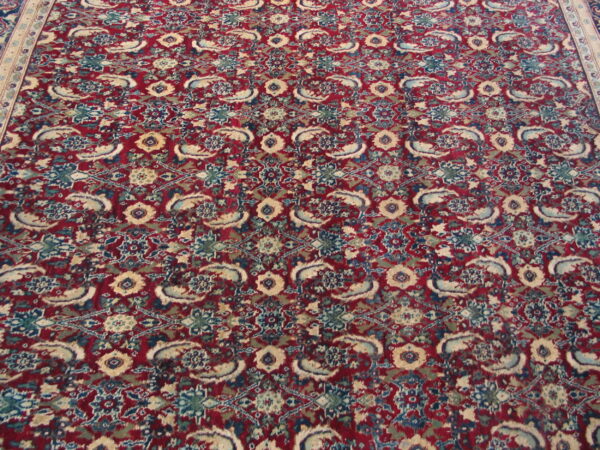 A traditional patterned rug featuring a red background with dense blue, teal, and cream motifs.