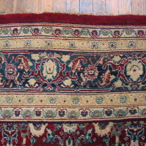 Ornate rug border featuring floral patterns in deep red, blue, and cream on distressed wood planks.