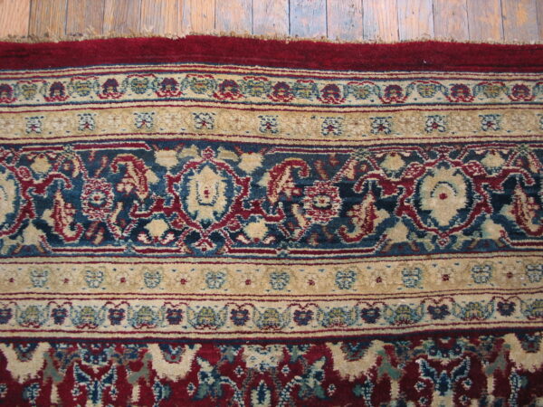 Ornate rug border featuring floral patterns in deep red, blue, and cream on distressed wood planks.