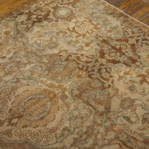 Beige and brown highly distressed ornate rug with subtle blue accents over wood flooring.
