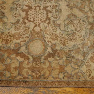Traditional rug in muted browns, beige, and faint blue details rests on distressed wood flooring.