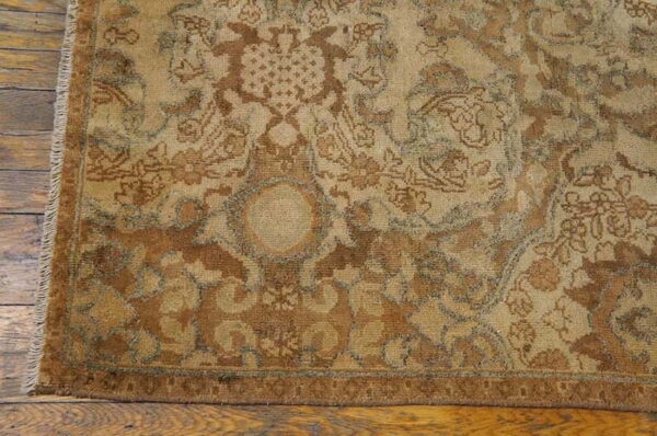 Traditional rug in muted browns, beige, and faint blue details rests on distressed wood flooring.