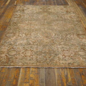 A monochromatic tan and brown ornate rug with low pile is displayed on dark, rustic wood flooring.