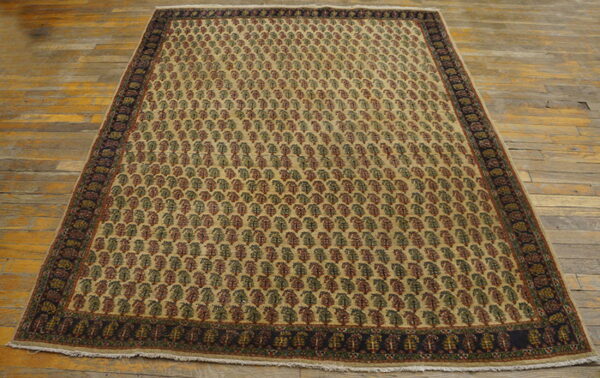 Traditional beige rug with red and green repeating patterns, a dark border, resting on worn wood floors.