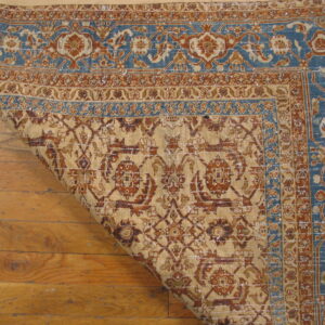 A patterned beige, rust, and blue rug is curled back over distressed wood flooring.