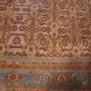 Beige rug featuring a dense geometric and floral pattern in rust and brown, highlighted by a teal border.