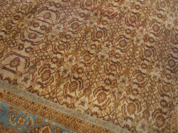 Beige rug field with an all-over intricate brown and rust floral pattern and a contrasting teal border.