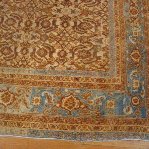 Muted gold and rust floral pattern rug with a distinct blue border resting on hardwood flooring.