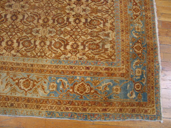 Muted gold and rust floral pattern rug with a distinct blue border resting on hardwood flooring.