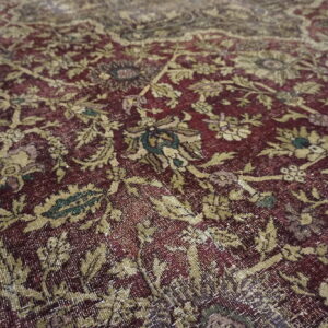The low-pile rug features a distressed maroon background with an intricate faded gold and green floral pattern.