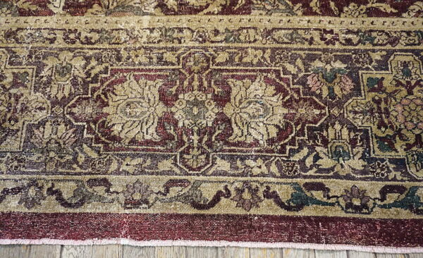 Ornate low-pile rug border in tan, deep red, and dark green, placed on light gray wood flooring.