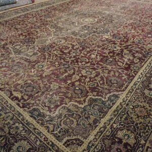 Low-pile area rug featuring dense traditional floral patterns in deep red, beige, and gold on a wood floor.