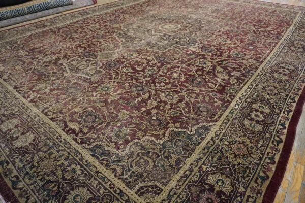 Low-pile area rug featuring dense traditional floral patterns in deep red, beige, and gold on a wood floor.
