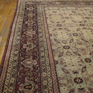 A pale green floral rug with dense burgundy and beige borders lies on polished light wood flooring.