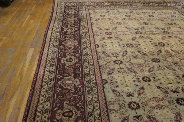 A pale green floral rug with dense burgundy and beige borders lies on polished light wood flooring.