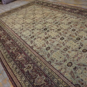 Oversized distressed rug featuring a light sage field and intricate burgundy and cream patterned border on wood floorboards.
