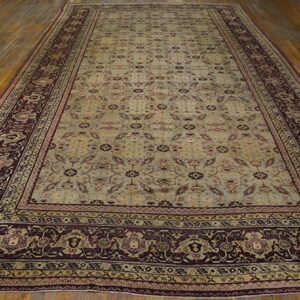 Pale green and maroon patterned rug with a wide dark border on distressed wood plank flooring.