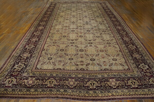 Pale green and maroon patterned rug with a wide dark border on distressed wood plank flooring.