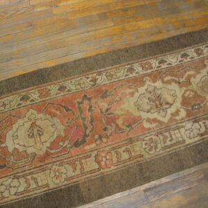 Traditional runner rug in terracotta, cream, and dark brown lies on worn wooden floorboards.