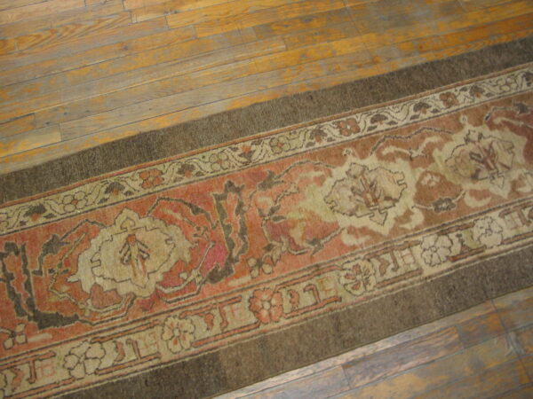 Traditional runner rug in terracotta, cream, and dark brown lies on worn wooden floorboards.