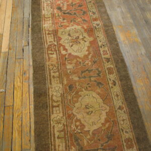 Rust and tan patterned runner rug with a dark border on rustic, wide-plank wood flooring.