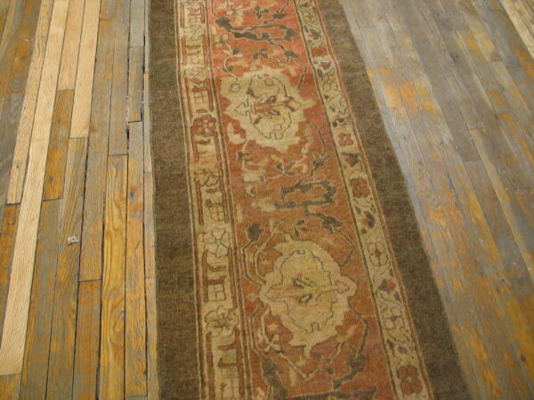 Rust and tan patterned runner rug with a dark border on rustic, wide-plank wood flooring.