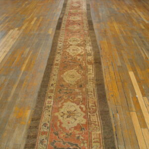 Ornate rust and beige runner rug on worn wooden floorboards, laid down the center of a room.