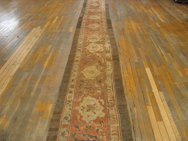 Ornate rust and beige runner rug on worn wooden floorboards, laid down the center of a room.